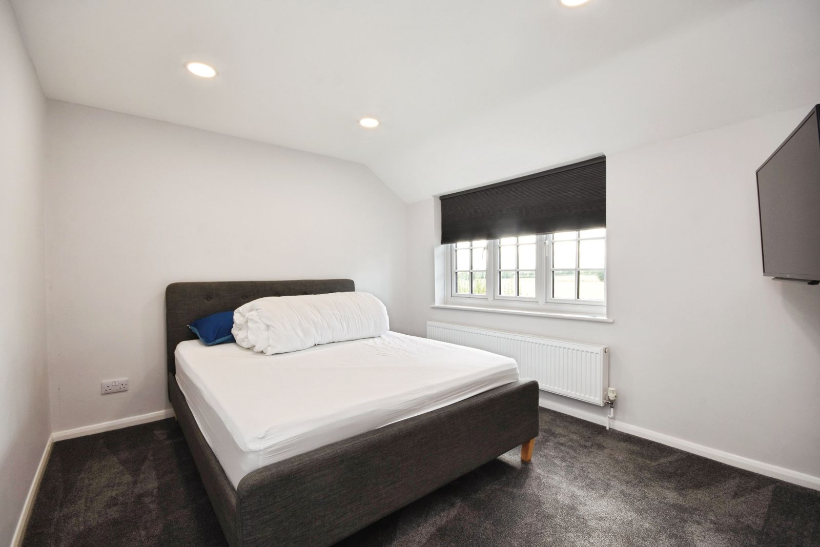 Second double bedroom with blackout blind and wall-mounted TV